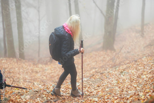 A woman with a backpack hiking through a foggy forest, surrounded by tall trees and mysterious mist swirling around her © Damian