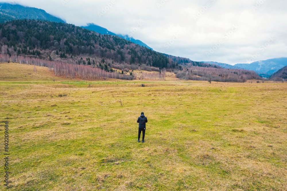 Fototapeta premium A person stands gracefully in a vast field, surrounded by majestic mountains in the distant background