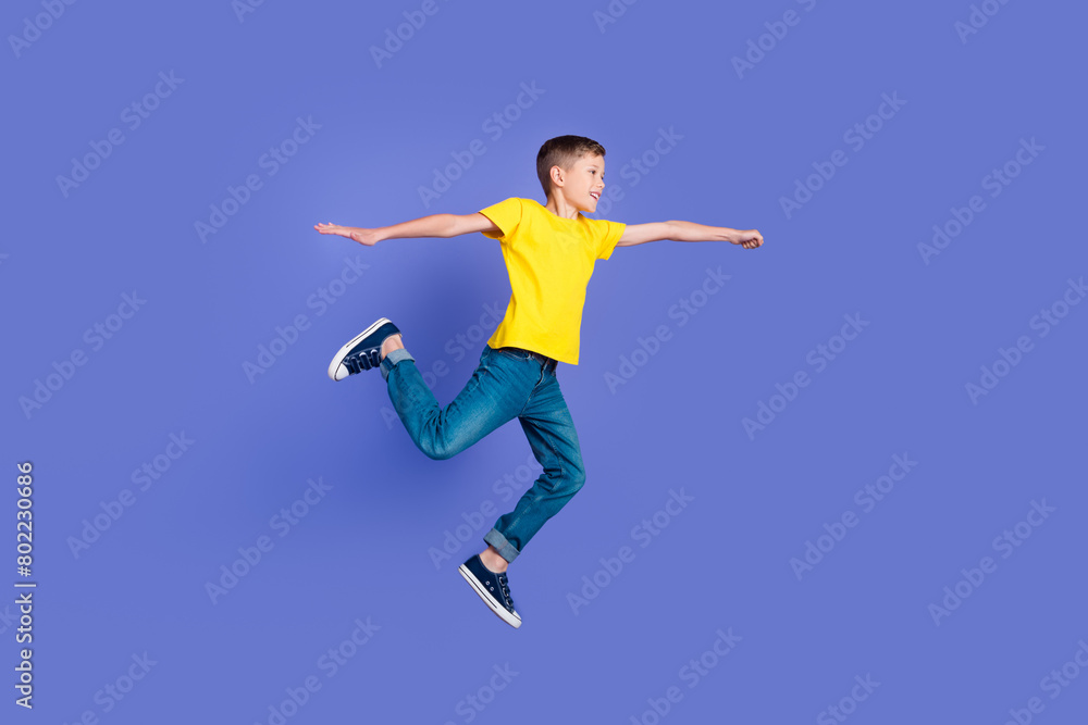 Full length photo of cheerful positive boy wear trendy yellow clothes have fun flight fly air isolated on violet color background