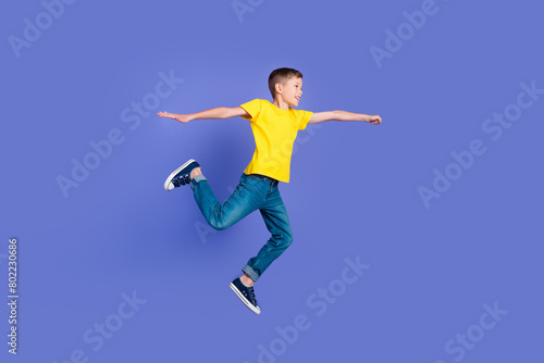 Full length photo of cheerful positive boy wear trendy yellow clothes have fun flight fly air isolated on violet color background