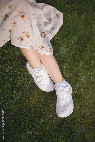 legs in light sneakers, green grass. Straight legs are relaxed on the grass. Female legs in sneakers and grass