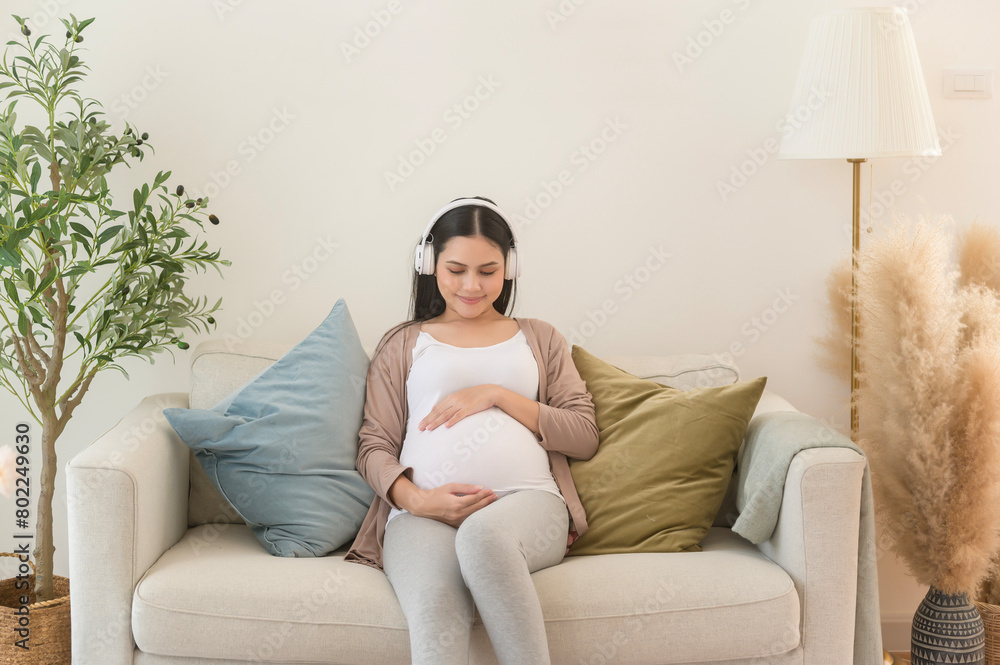 Happy pregnant woman with headphones listening to mozart music and lying on sofa, pregnancy concept