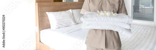 Hands of hotel maid putting plumeria flower and towels on the bed in the luxury hotel room ready for tourist travel