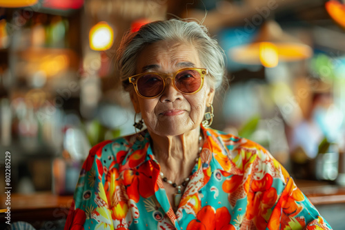 Elderly asian woman at a beach bar, relishing the sea breeze while sipping on a beverage, happiness. © Pavel