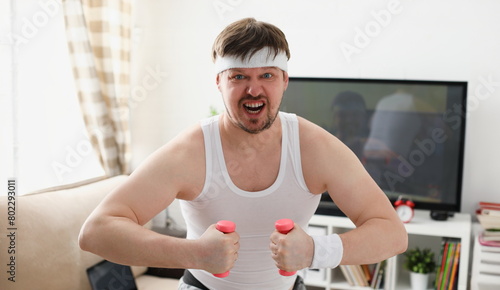 Young attractive man engaged in fitness at home holding dumbbell in hand trying to fight excess weight and loss photo