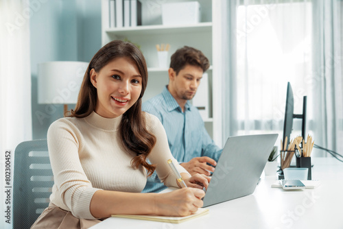 Smiling beautiful woman working on laptop aligning taking note to pose for looking at camera photo shooting portrait profile's business with smart coworker at modern office at morning time. Postulate.