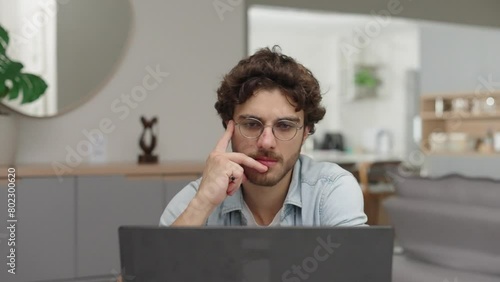 Thoughtful young businessman sitting at remote workplace with laptop computer. Pensive professional thinking at table in office. Focused business man face looking around. Serious man portrait
