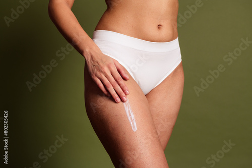No filter cropped photo of lady hips underwear lingerie applying skin cream isolated khaki color background