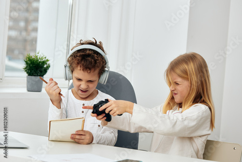 Happy siblings playing and blogging together indoors The two Caucasian teenagers, a boy and a girl, are sitting in their cozy home interior, smiling and holding their smartphones The connection of photo