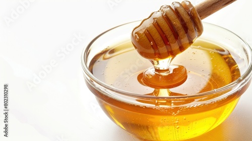 A glass bowl of clear golden brown honey isolated on a white background, honey dripping from a wooden honey clip.