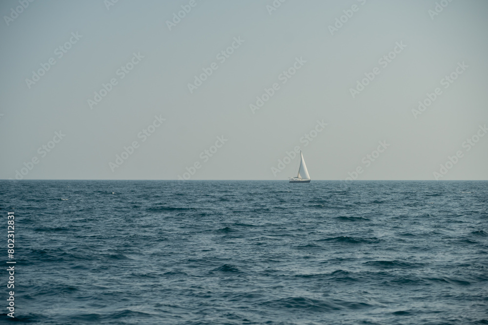 A yacht with white sails sails on the horizon of the choppy sea. Clear sky without clouds. Sailing voyages on a sailboat, regatta. A yacht with white sails sails on the horizon of the choppy sea. Clear sky without clouds. Sailing voyages on a sailboat, regatta.