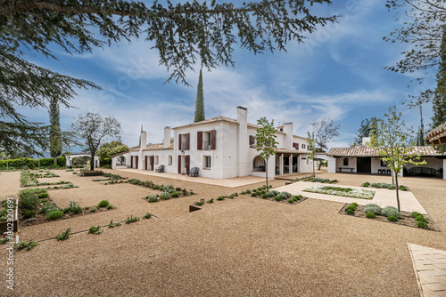 a beautiful Andalusian style country house with white walls, gravel paths and a variety of newly planted plants in the garden on a day with beautiful blue skies