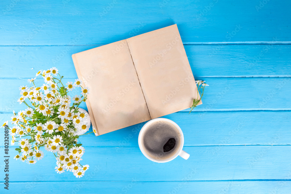 Fototapeta premium Chamomile daisy flowers bouquet, book, tea or coffee cup, relaxation holiday simple life enjoy summer background, on light blue wood background, top view copy space. Good day, good morning wishing