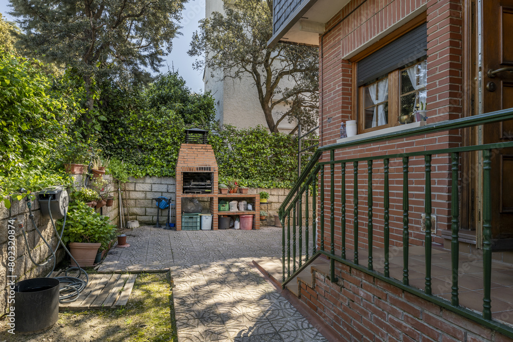Perimeter garden with tiled path around a single-family house with brick facades with hoses and barbecues on the wall Perimeter garden with tiled path around a single-family house with brick facades with hoses and barbecues on the wall