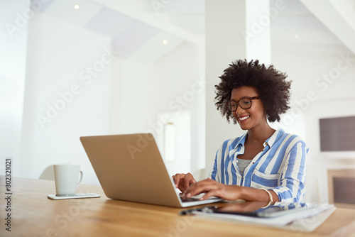 Happy woman, laptop and work from home for blog, social media and research at desk. African female journalist, technology and typing for networking, newspaper article and online magazine in house photo