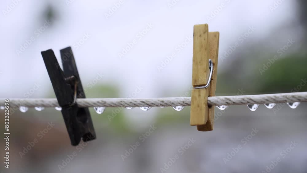 Two wooden clothespins hanging on a white cable covered in raindrops on a fully rainy day Two wooden clothespins hanging on a white cable covered in raindrops on a fully rainy day
