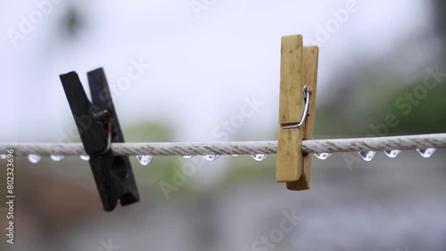 Two wooden clothespins hanging on a white cable covered in raindrops on a fully rainy day