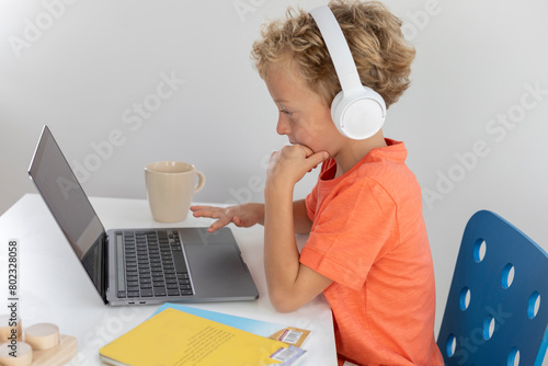 Little boy with white headphones and blonde hair, interacts with a laptop