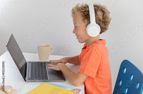 Little boy with white headphones and blonde hair, plays and has fun with a laptop
