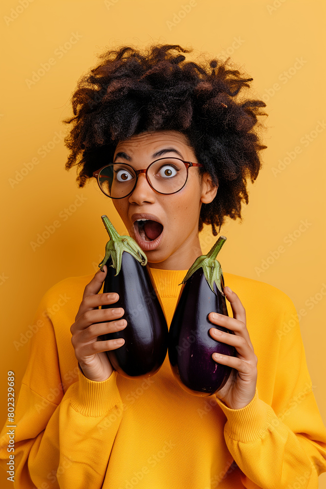 two eggplants in the hands of a shocked girl on a yellow background two eggplants in the hands of a shocked girl on a yellow background
