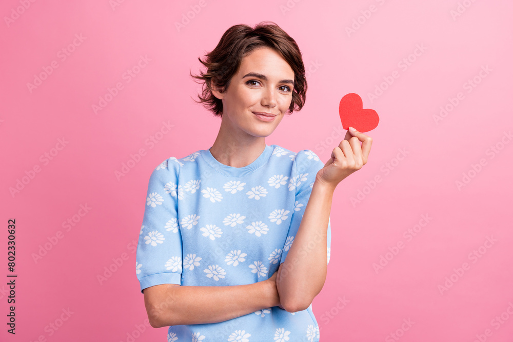 Photo of positive friendly lady hand hold small red paper heart symbol card isolated on pink color background Photo of positive friendly lady hand hold small red paper heart symbol card isolated on pink color background