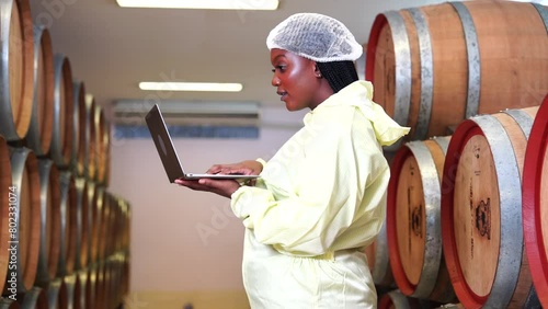 Black female technician holding laptop are experts in wine quality inspection visit to inspect the quality of grape fermentation tanks and check the temperature of wine in the factory. photo