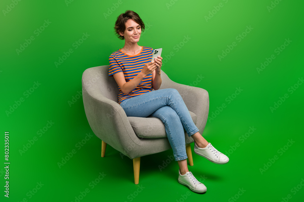 Full size portrait of lovely gorgeous girl sit cozy chair use smart phone texting isolated on green color background Full size portrait of lovely gorgeous girl sit cozy chair use smart phone texting isolated on green color background
