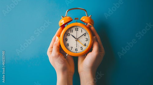 Female hand holding a alarm clock with blue background.