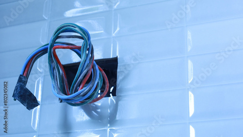 Electrical wires in holes in tiled walls. Closeup of a group of colorful wires for installing electronic equipment on a bathroom wall with wires protruding in a house under construction. Select focus