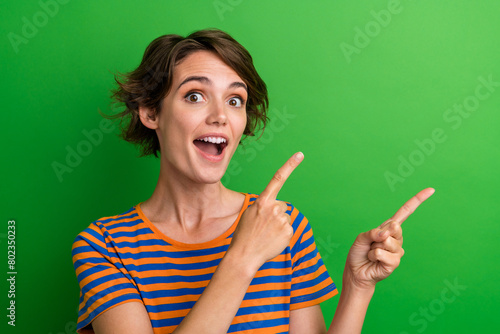 Photo portrait of lovely young lady excited point empty space dressed stylish striped garment isolated on green color background