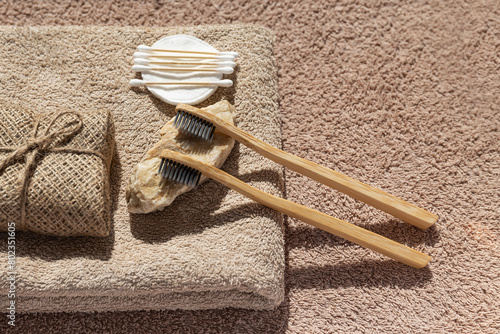 Creative layout made of two toothbrushes, natural soap, cootton buds and pads on sunlit background with towels. Morning routine concept.