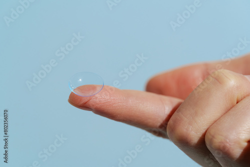 Finger of female hand holding blue transparent contact lens while wearing on blue isolated background. Vision improvement concept, farsightedness and nearsightedness, ophthalmologist. photo