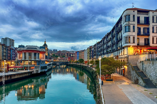Colorful residential and apartment buildings and restaurants along the Nervion River in Bilbao, Spain on a cloudy sunset photo