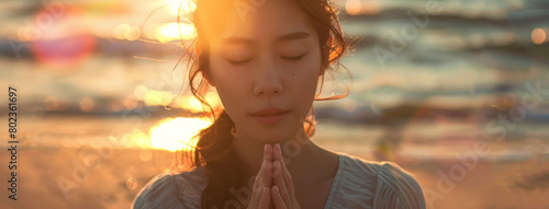 Asian woman, peace and beach with praying at sunset for spiritual, worship in nature for meditation. Female person, calm and ocean with hands for God in banner, faith and mindfulness with prayer