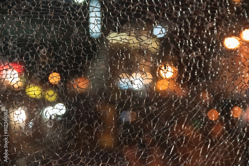 Uniform texture of geometric pattern of broken glass and bullet holes against the background of night city lights