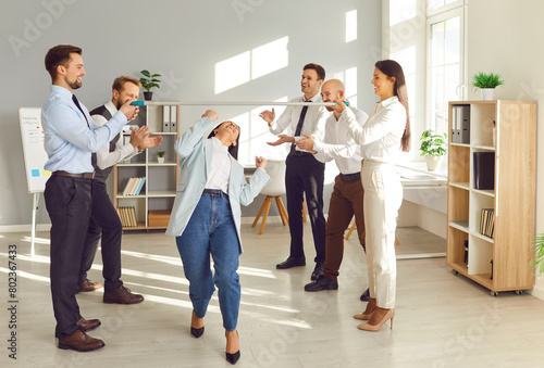 Group of happy funny young business people company employees having fun organizing competitions between coworkers in office with a stick. Teamwork  corporate team building and success concept.