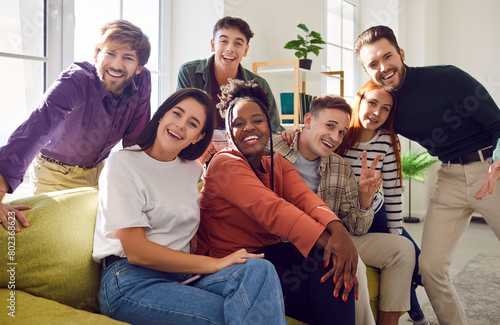 Portrait of a group of happy young diverse friends men and women sitting on sofa in the living room at home looking cheerful at camera enjoying meeting. Friendship  party and home leisure concept.