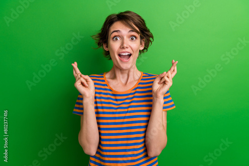 Photo portrait of lovely young lady impressed fingers crossed gesture dressed stylish striped garment isolated on green color background
