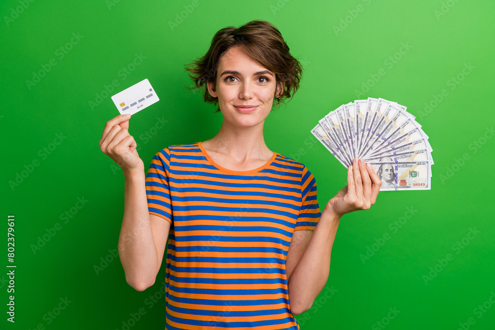 Photo portrait of attractive young woman hold credit card money fan dressed stylish striped clothes isolated on green color background Photo portrait of attractive young woman hold credit card money fan dressed stylish striped clothes isolated on green color background
