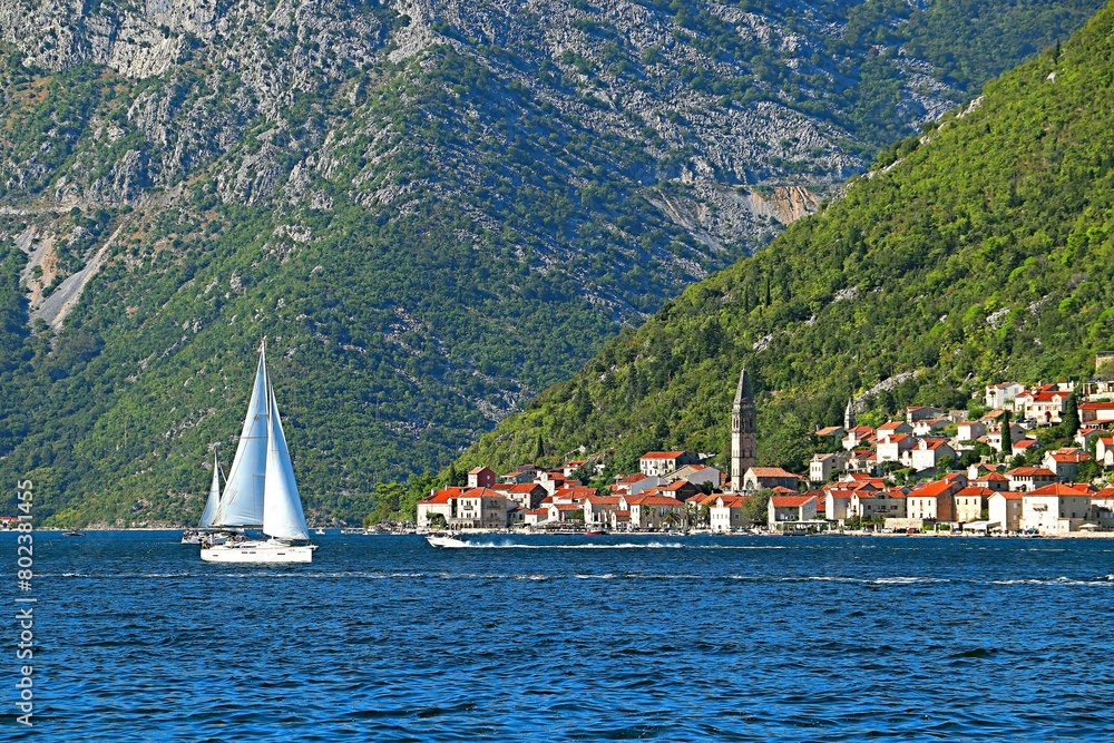 Sailing yacht in the Bay of Kotor of the Adriatic Sea against the backdrop of mountains and a resort village