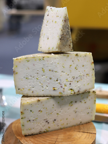 cuñas y mitades de quesos artesanales con ingrediente de pistacho en una tabla de madera en el mercado