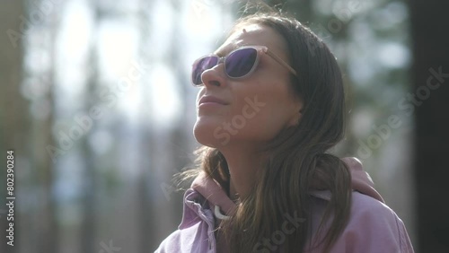 Portrait of Young Beautiful Woman with Long Brunette Hair Exhaling Fresh Air, Taking Deep Breath and Reducing Stress. Happy female woman in sunglasses enjoying walk in the sunny spring parkland