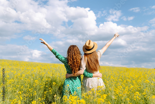 Two beautiful women in the middle of a yellow rapeseed field. Nature, vacation, relax and lifestyle. Summer landscape.