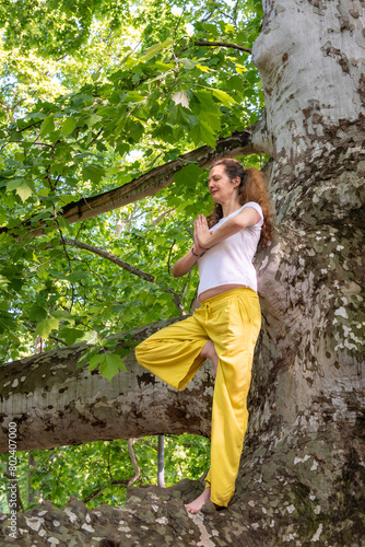Beautiful woman with gorgeous curly hair doing yoga in nature, dressed in white and yellow combination, concept: active healthy life, in love with nature, support, balance, wellbeing, energy