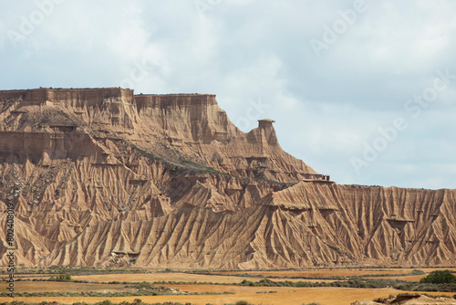 A large mountain range with a rocky, barren landscape. The sky is cloudy and the sun is shining