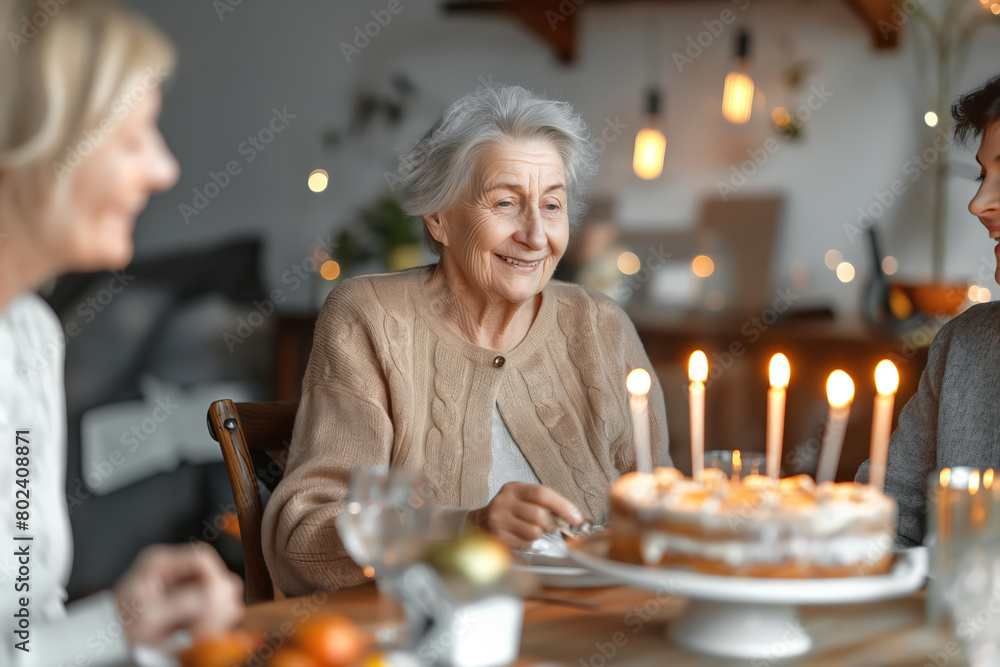 Happy elderly woman with her family at festive table with cake and candles celebrates her birthday