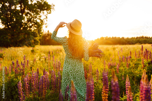 Beautiful woman holding bouquet of lavender flowers walking in summer meadow. Fashion, beauty, nature concept. Collection of medicinal herbs.