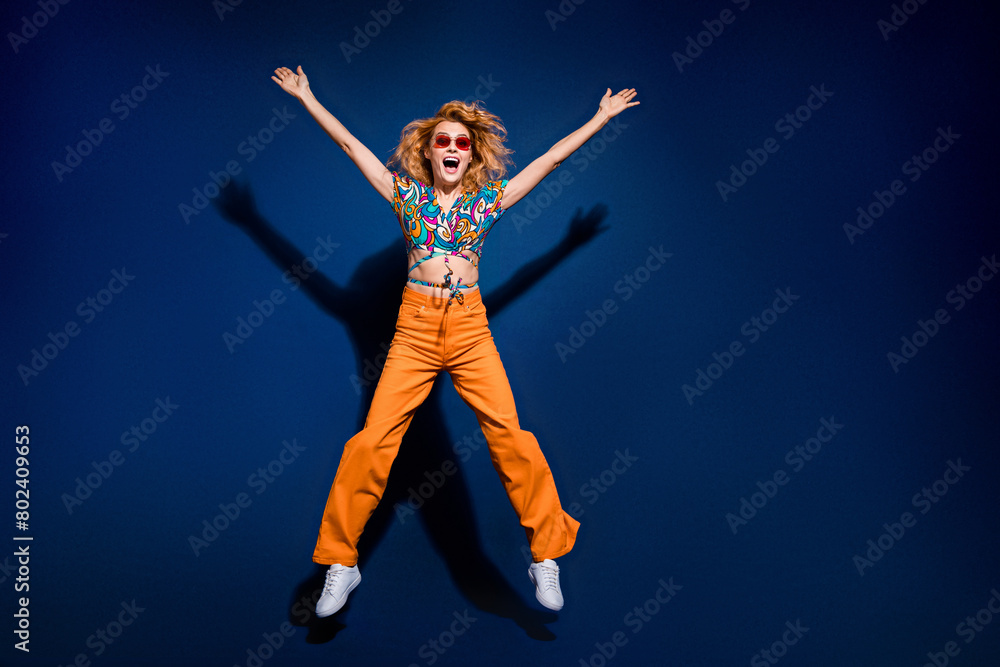 Full size photo of pretty young woman jump raise hands empty space wear top isolated on dark blue color background