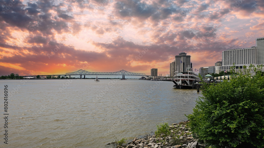Obraz premium a gorgeous spring landscape along the MIssissippi River with boats sailing and the Crescent City Connection bridge with hotels and office buildings in the city skyline n New Orleans Louisiana USA