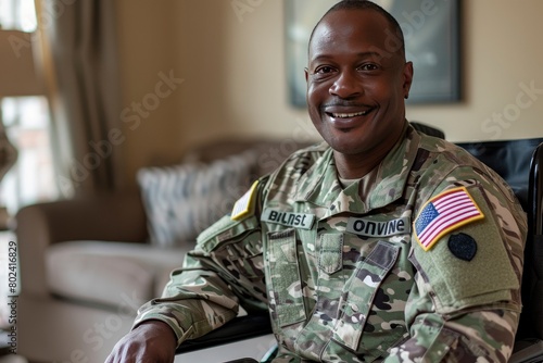 Black man in a military uniform sitting in a wheelchair smiling at the camera, with a living room background